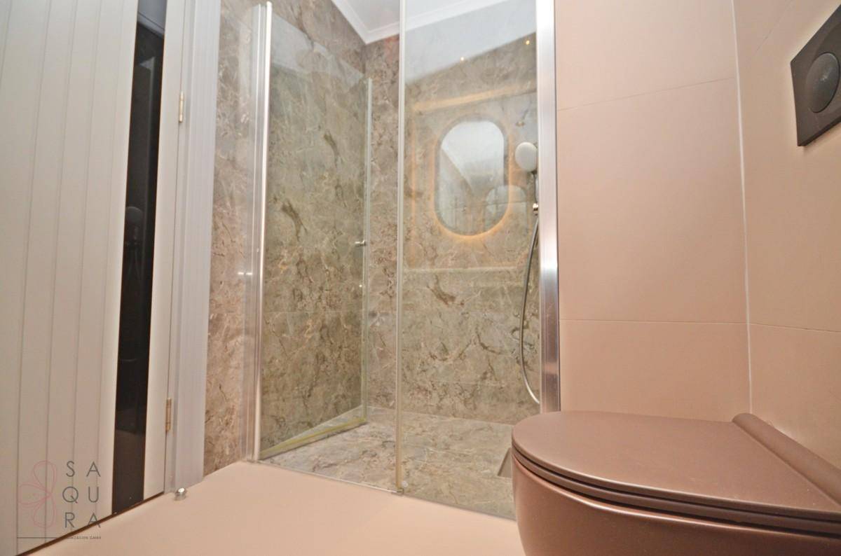 Modernes Badezimmer mit begehbarer Dusche, Glasabtrennung und Wand-WC.