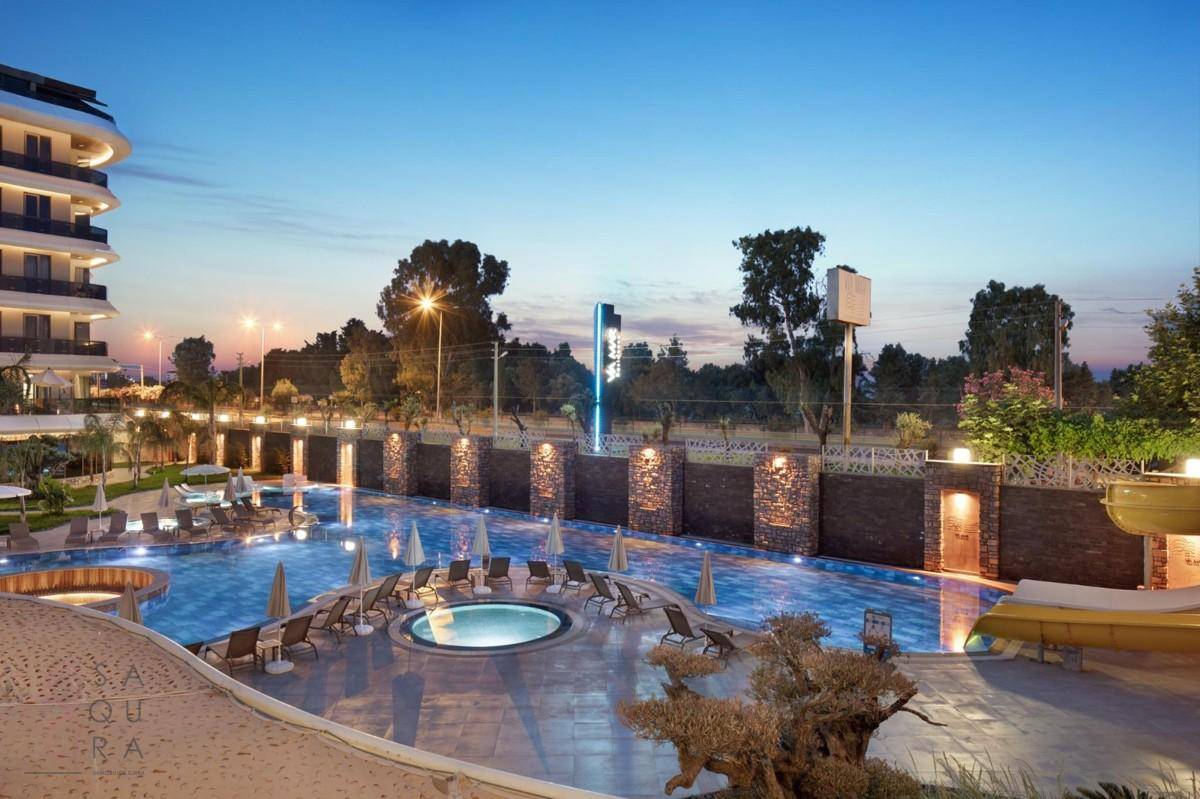 Abendliche Ansicht des modernen Gebäudes mit beleuchtetem Poolbereich, Whirlpool und Wasserrutsche.