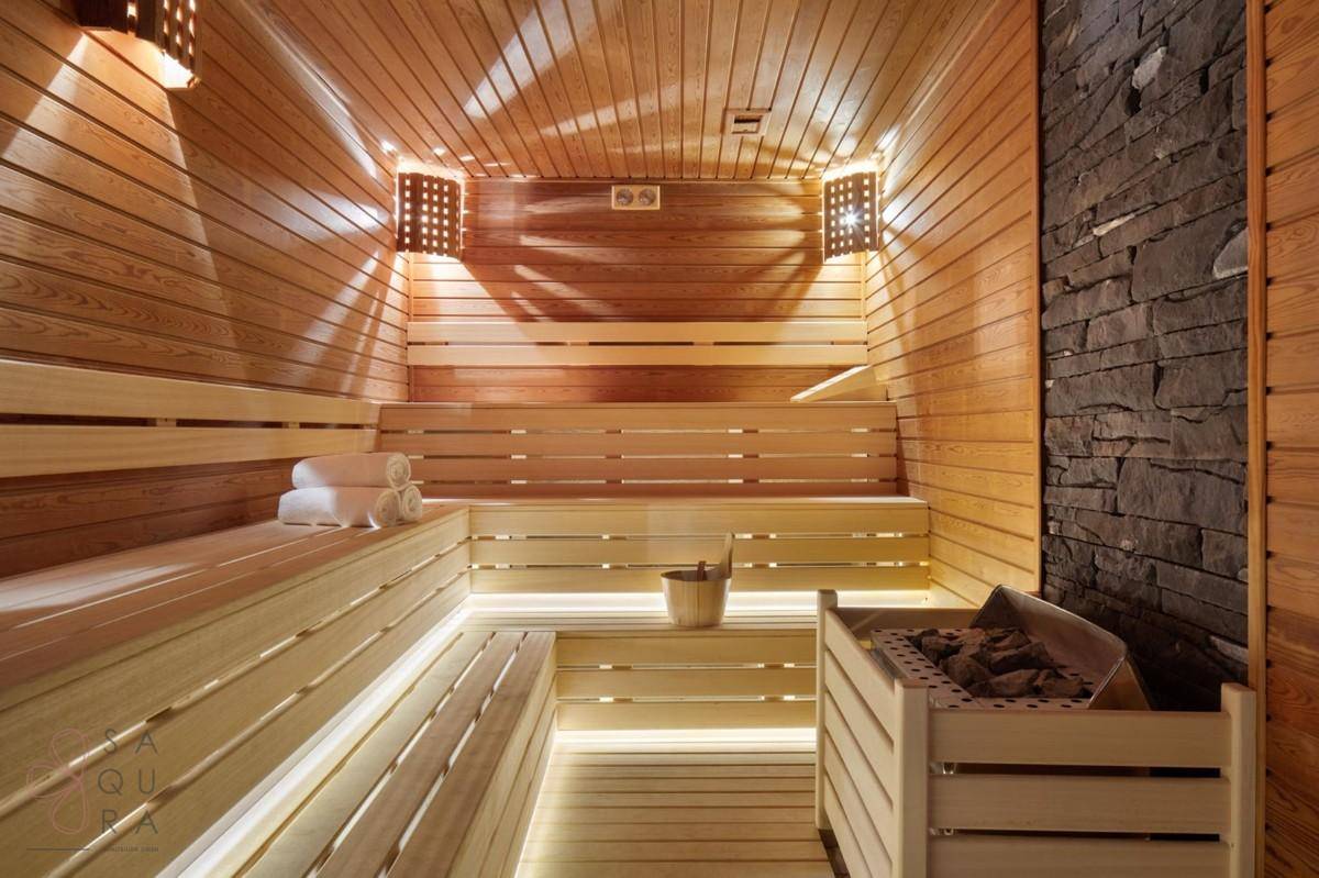 Traditionelle Holzsauna mit mehreren Bänken, Steinofen und indirekter Beleuchtung.