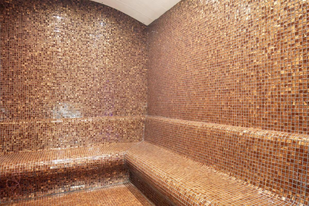 Dampfbad mit kleinen Mosaikfliesen und integrierten Sitzbänken für Entspannung.
