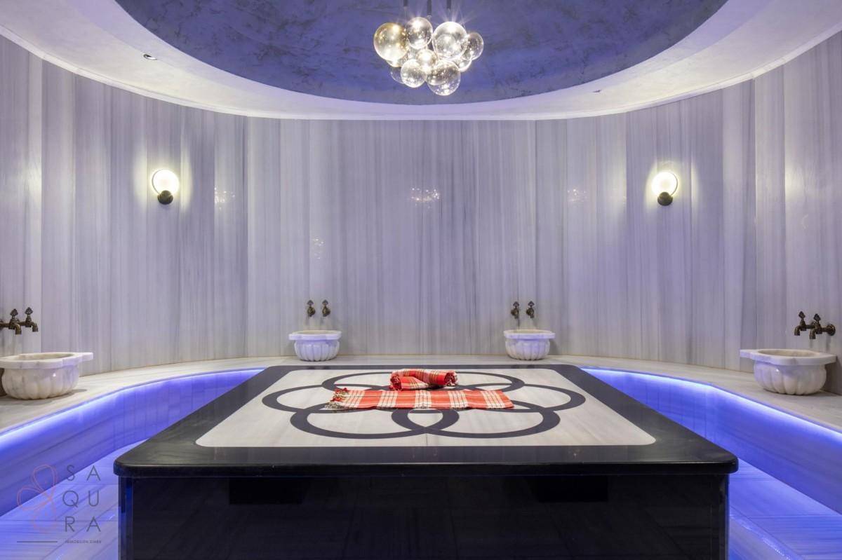 Luxuriöses Hamam mit Marmoroberflächen, zentraler Liegefläche und indirekter Beleuchtung.