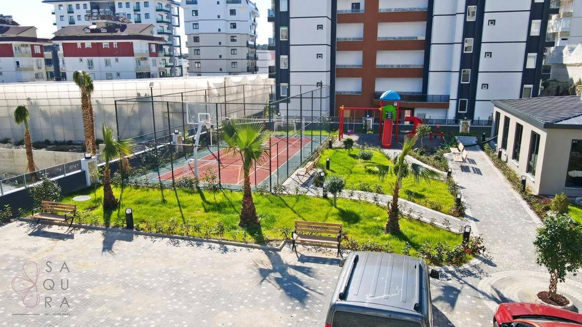 Sport- und Spielbereich der Wohnanlage mit Basketballplatz, Kinderspielplatz und Bänken.