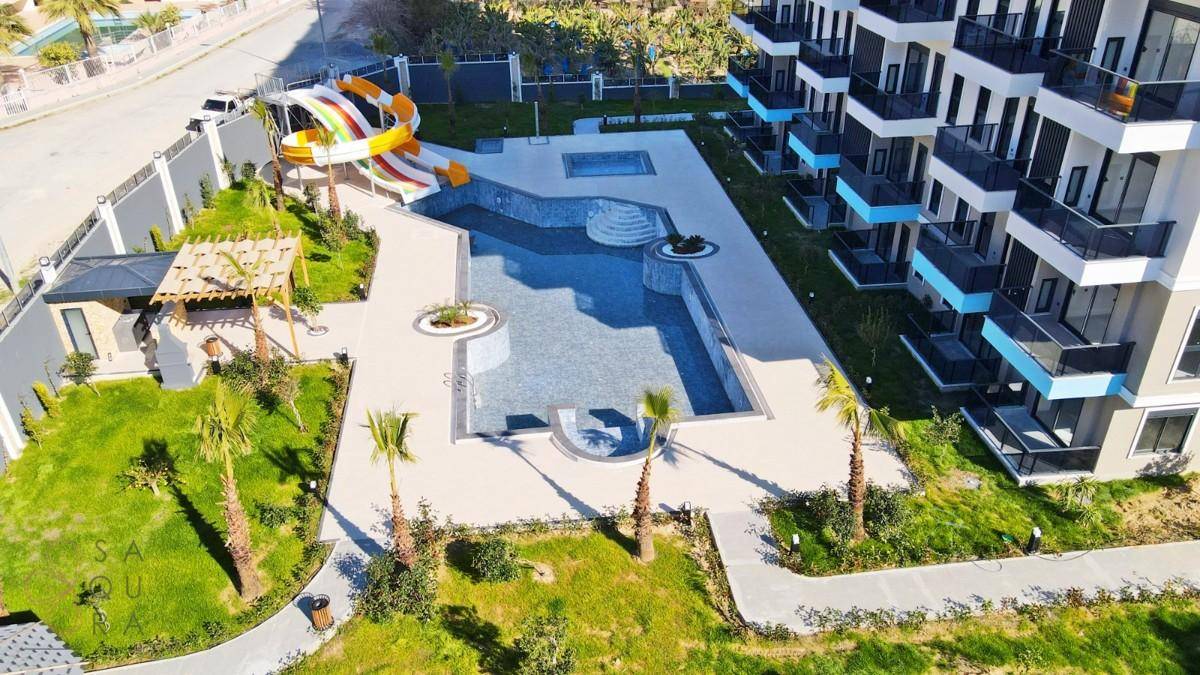 Außenbereich der Wohnanlage mit großem Pool, Wasserrutsche und Palmen im Garten.