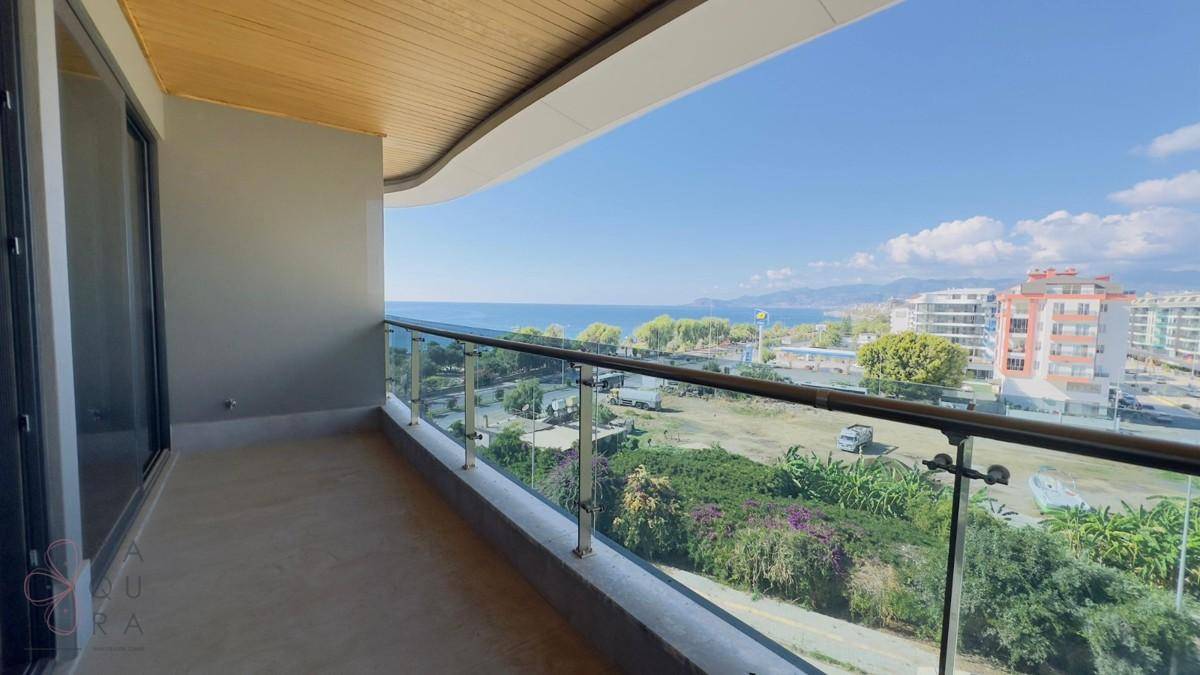 Geräumiger Balkon mit Glasgeländer und weitem Blick auf das Meer und die Küstenlandschaft.