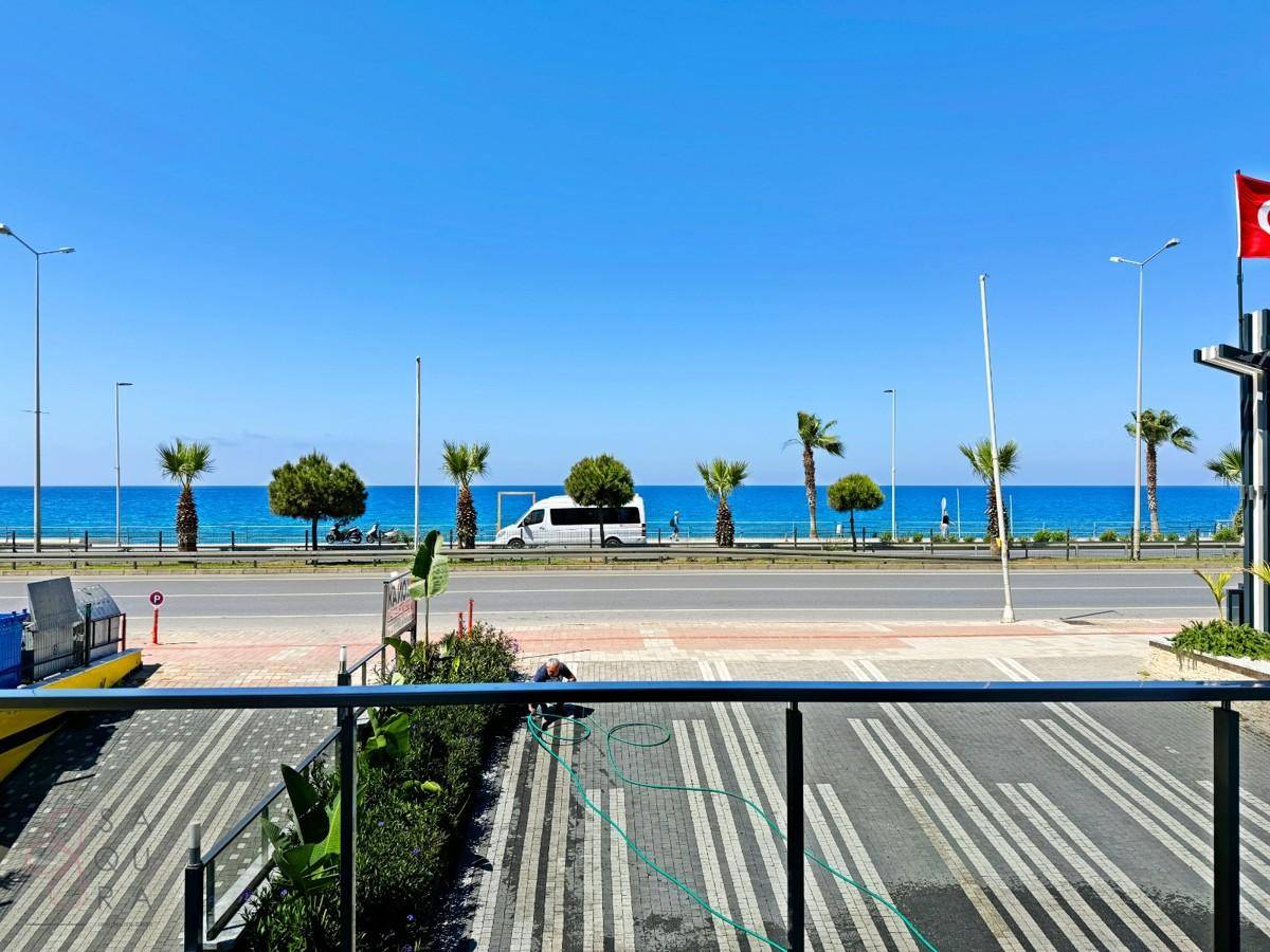 Panoramablick auf das Meer mit Palmen und einer Küstenstraße unter strahlend blauem Himmel.