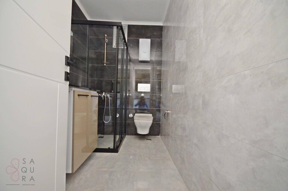 Modernes Badezimmer mit grauen Fliesen, wandhängendem WC und einer geräumigen Duschkabine.