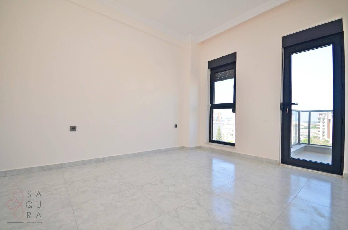 Helles, unmöbliertes Zimmer mit Fliesenboden, Fenster und Zugang zu einem kleinen Balkon.