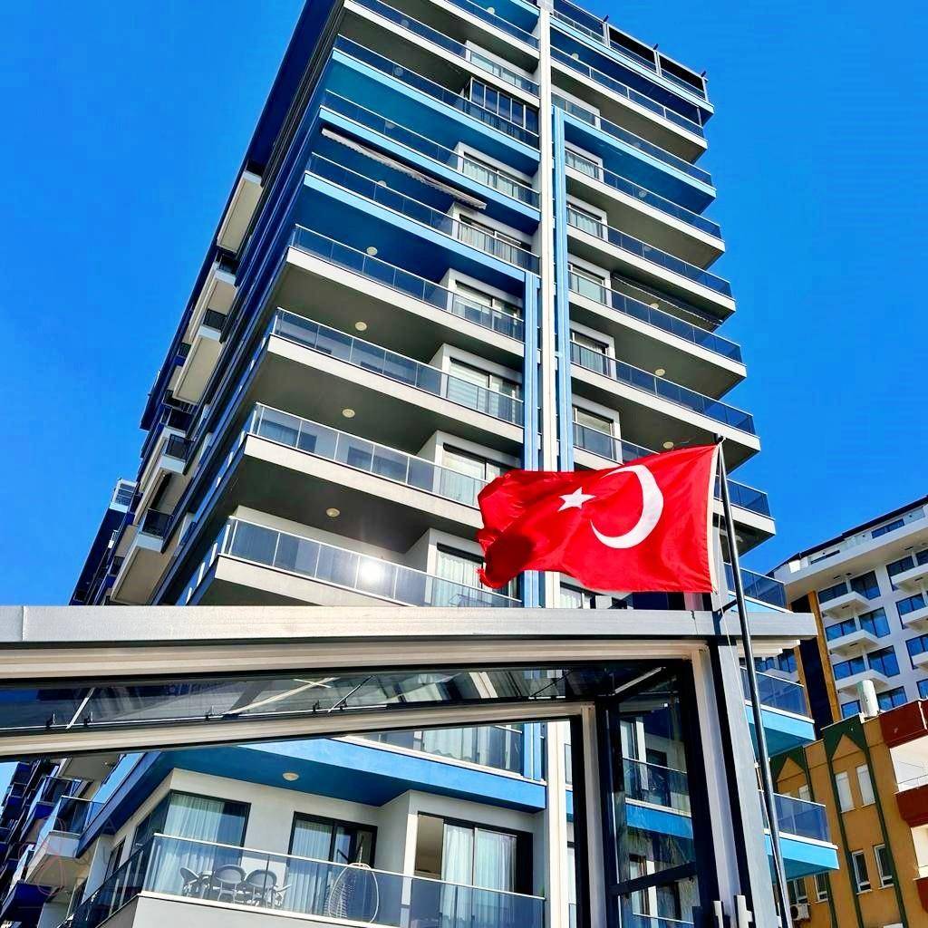 Modernes Hochhaus mit blauen Balkonen und einer wehenden türkischen Flagge unter blauem Himmel.