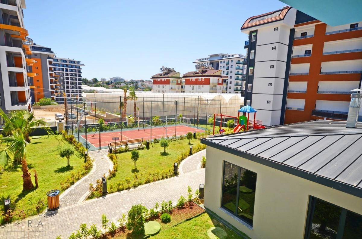 Gemeinschaftlicher Außenbereich mit Tennisplatz, Kinderspielplatz und gepflegten Grünflächen zwischen Wohngebäuden.