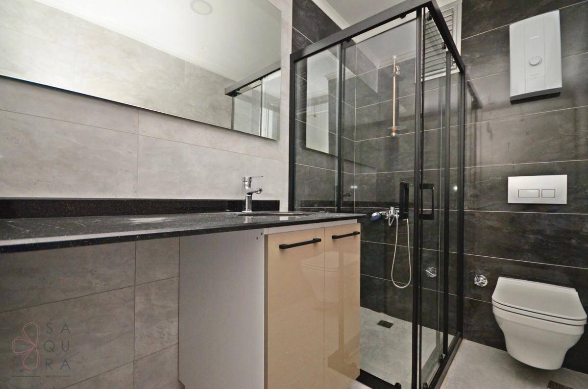 Modernes Badezimmer mit grauen Fliesen, Waschtisch mit Einzelwaschbecken und großer Duschkabine.