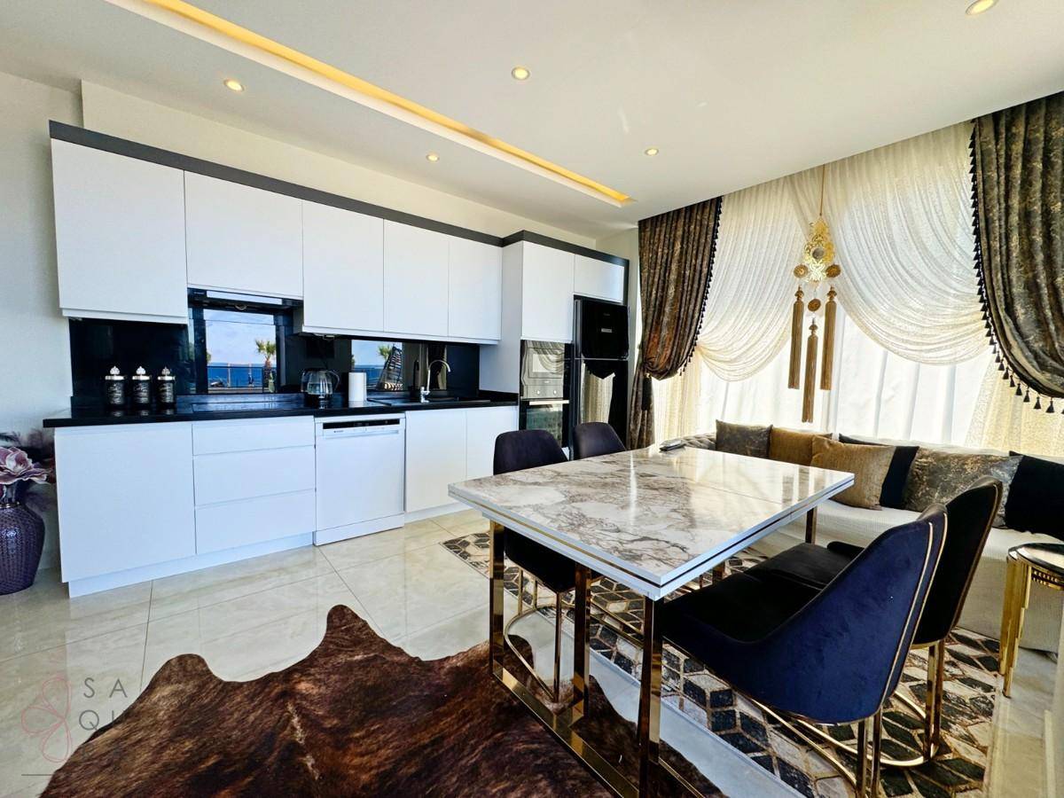 Moderne offene Küche mit weißen Schränken, schwarzer Arbeitsplatte und eleganten Vorhängen.