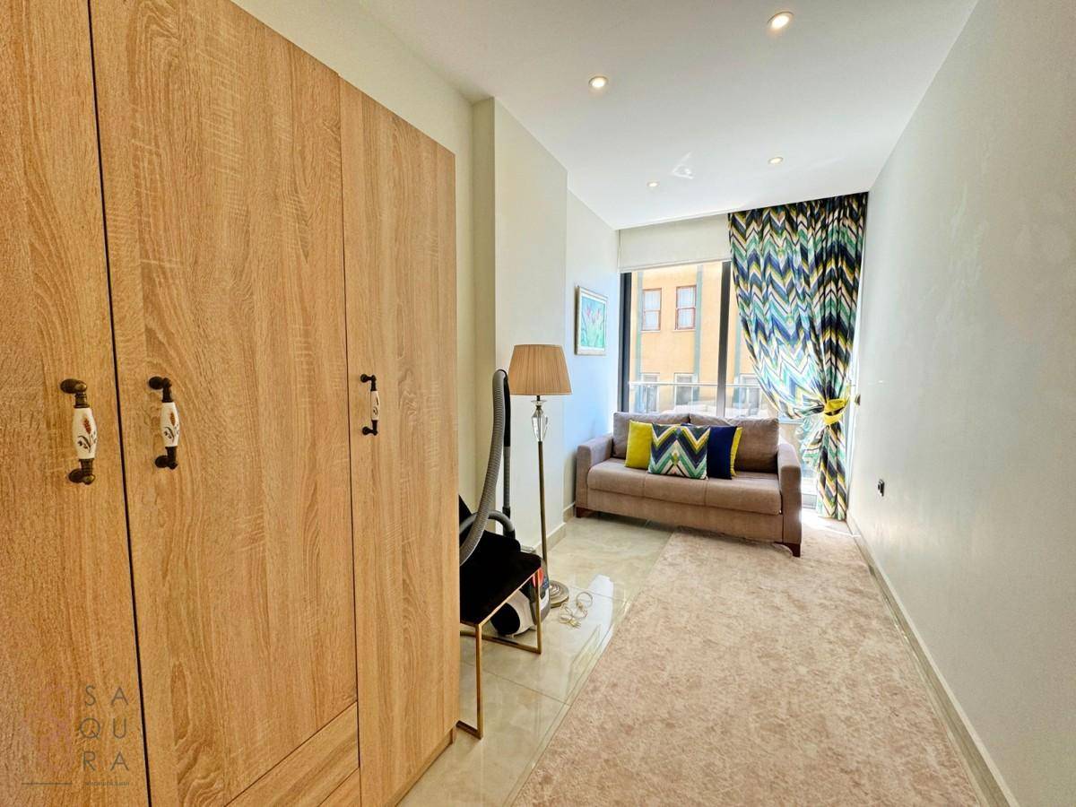 Helles Zimmer mit Holzschrank, kleinem Sofa und farbenfrohen Vorhängen am Fenster.