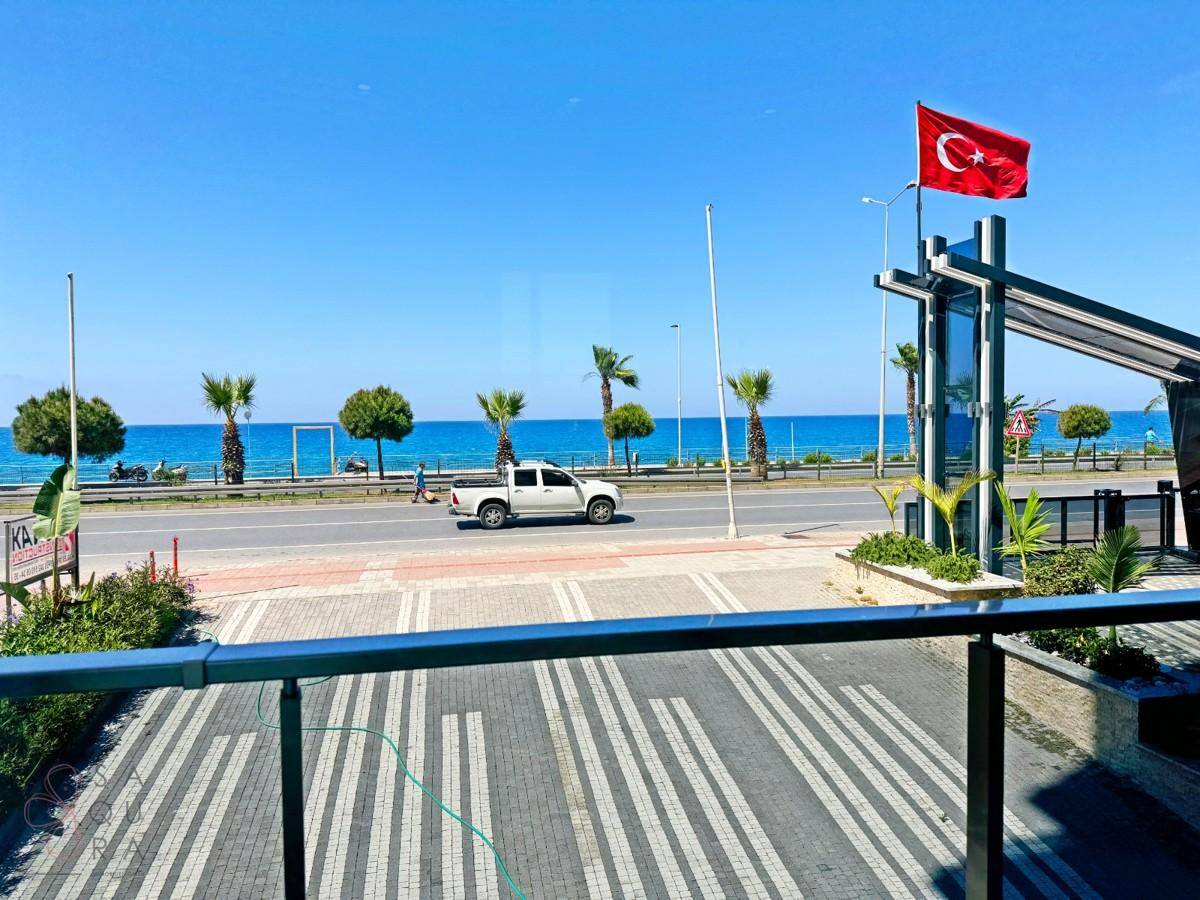 Weitläufiger Blick auf das Meer mit Palmen und einer belebten Küstenstraße an einem sonnigen Tag.
