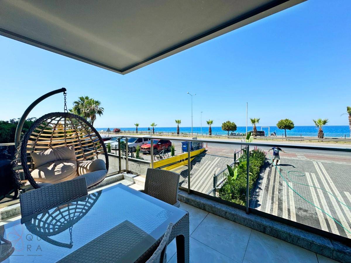 Möblierter Balkon mit Hängesessel und Esstisch, bietet einen weiten Blick auf das Meer.