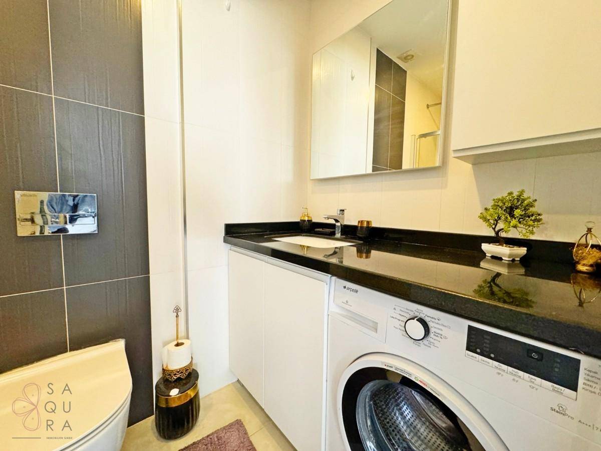 Modernes Badezimmer mit Waschbecken, Spiegelschrank, Toilette und integrierter Waschmaschine.