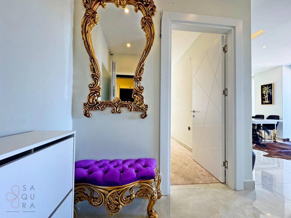Eleganter Flur mit einem opulenten goldenen Spiegel und einer lila gepolsterten Sitzbank.
