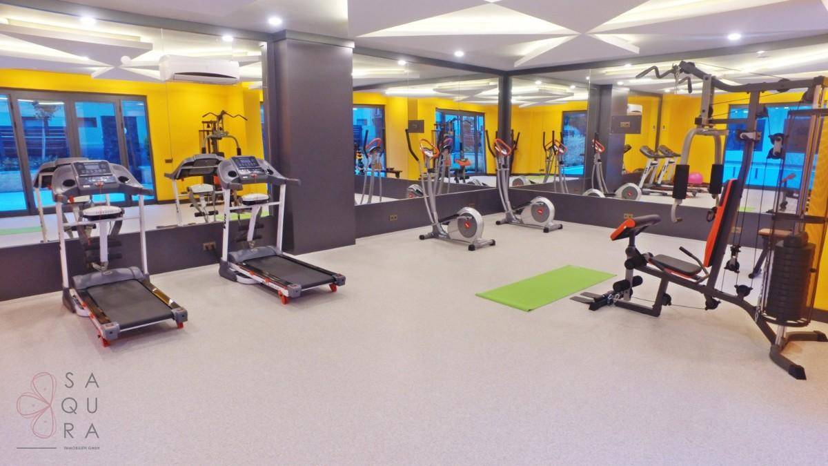 Gut ausgestatteter Fitnessraum mit verschiedenen Trainingsgeräten und großen Spiegeln.