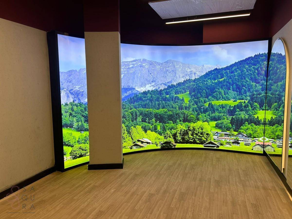 Raum mit großen digitalen Bildschirmen, die eine malerische Berglandschaft zeigen.