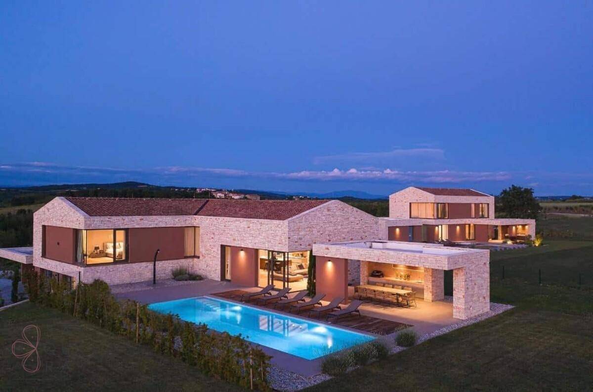 Luftaufnahme des Villenkomplexes bei Dämmerung mit beleuchteten Pools und weitläufiger Landschaft.