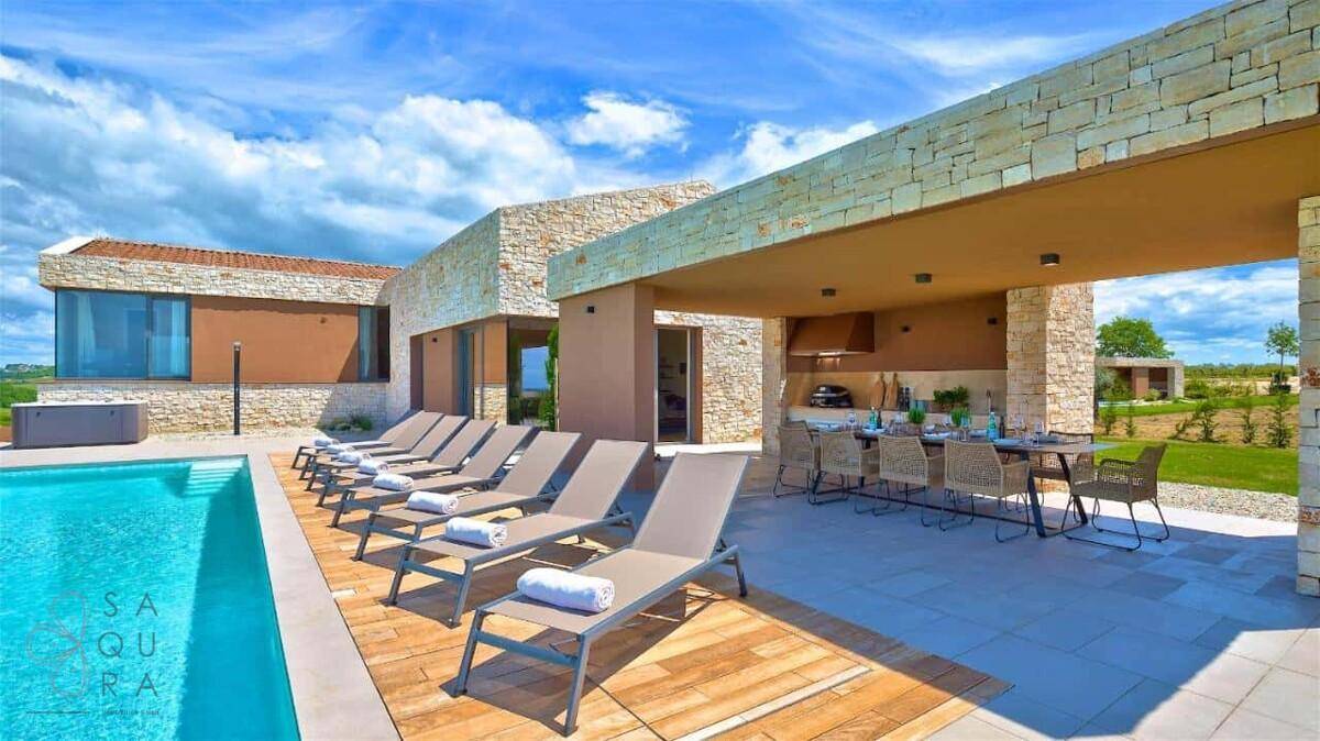 Weitläufige Terrasse mit Pool, zahlreichen Sonnenliegen und einem überdachten Essbereich.