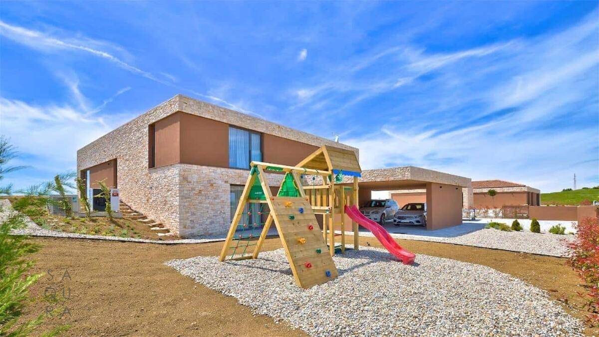 Moderne Villa mit Kinderspielplatz und überdachtem Carport für zwei Fahrzeuge.