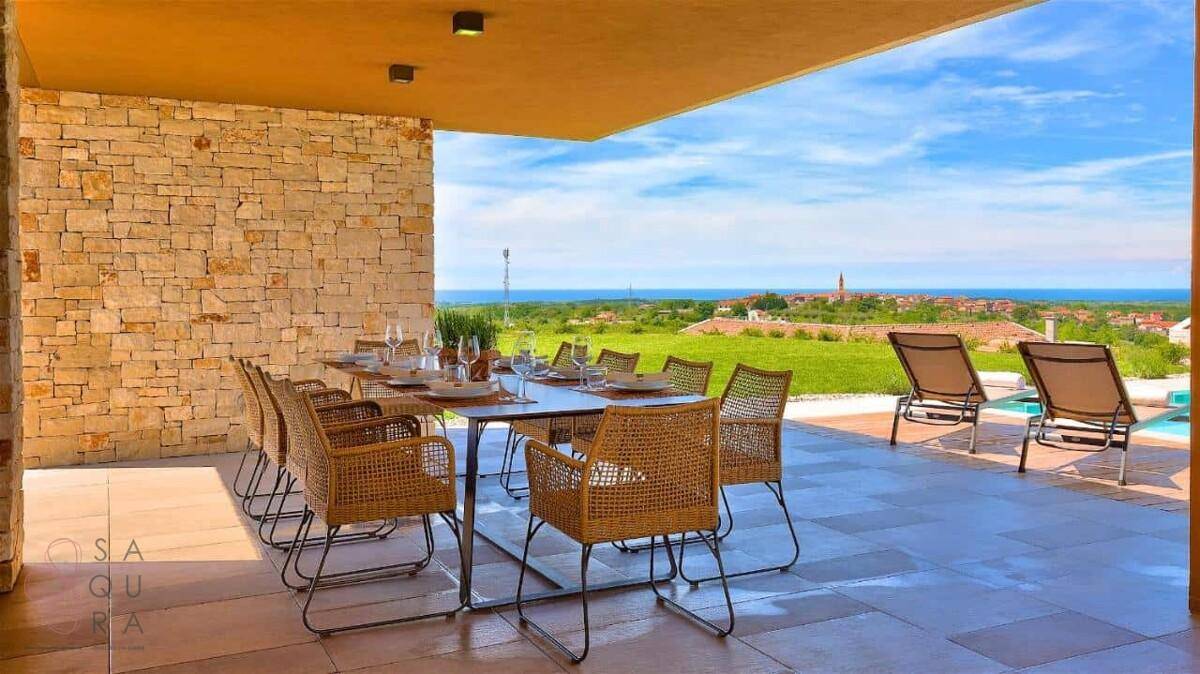 Überdachter Essbereich im Freien mit Korbstühlen und weitem Blick auf die Landschaft und das Meer.
