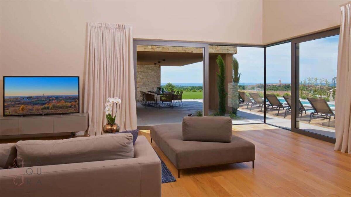 Helles Wohnzimmer mit Holzboden und großen Glasfronten, die zur Terrasse und zum Pool führen.