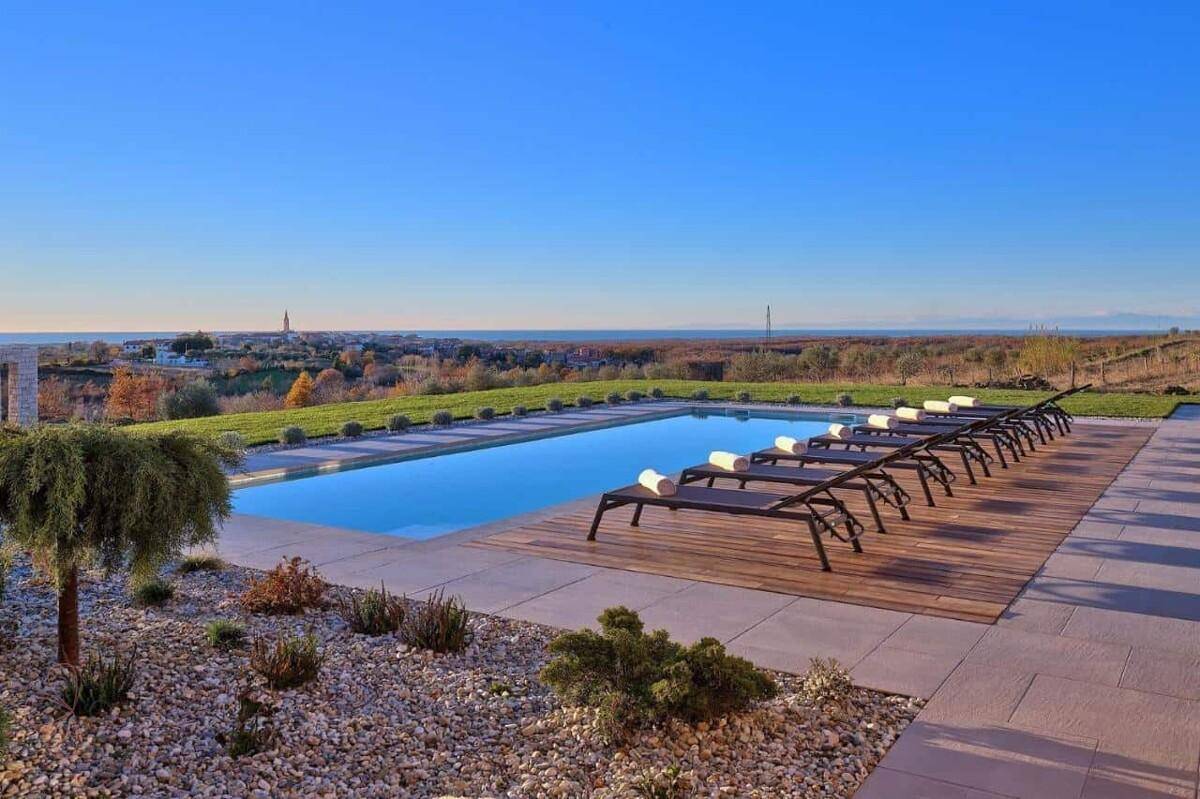 Langer Swimmingpool mit Sonnenliegen und Panoramablick auf die Küste und das Meer.