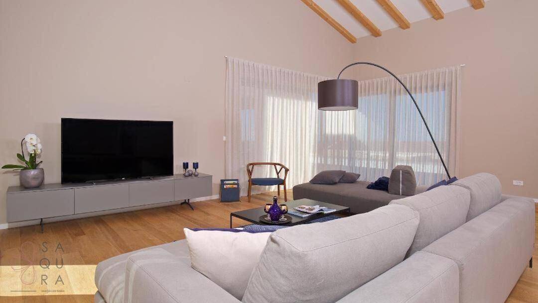 Geräumiges Wohnzimmer mit bequemer Couch, großem Fernseher und viel natürlichem Licht.