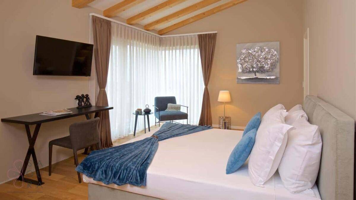 Helles Schlafzimmer mit Doppelbett, Schreibtisch und großen Fenstern mit Holzbalkendecke.