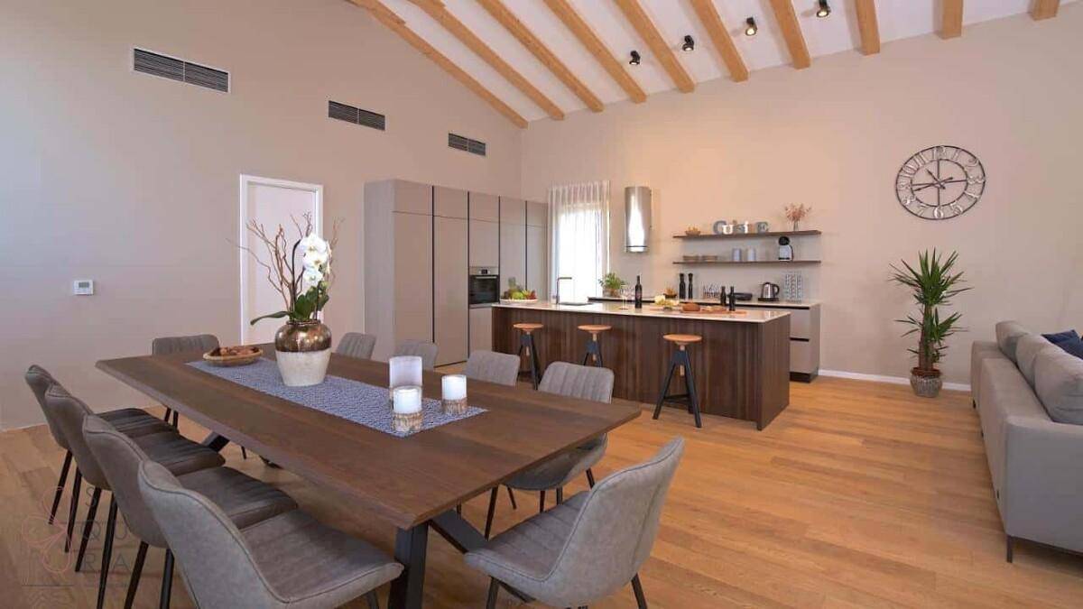 Moderner Essbereich mit großem Holztisch und offener Küche mit Insel und Barhockern.