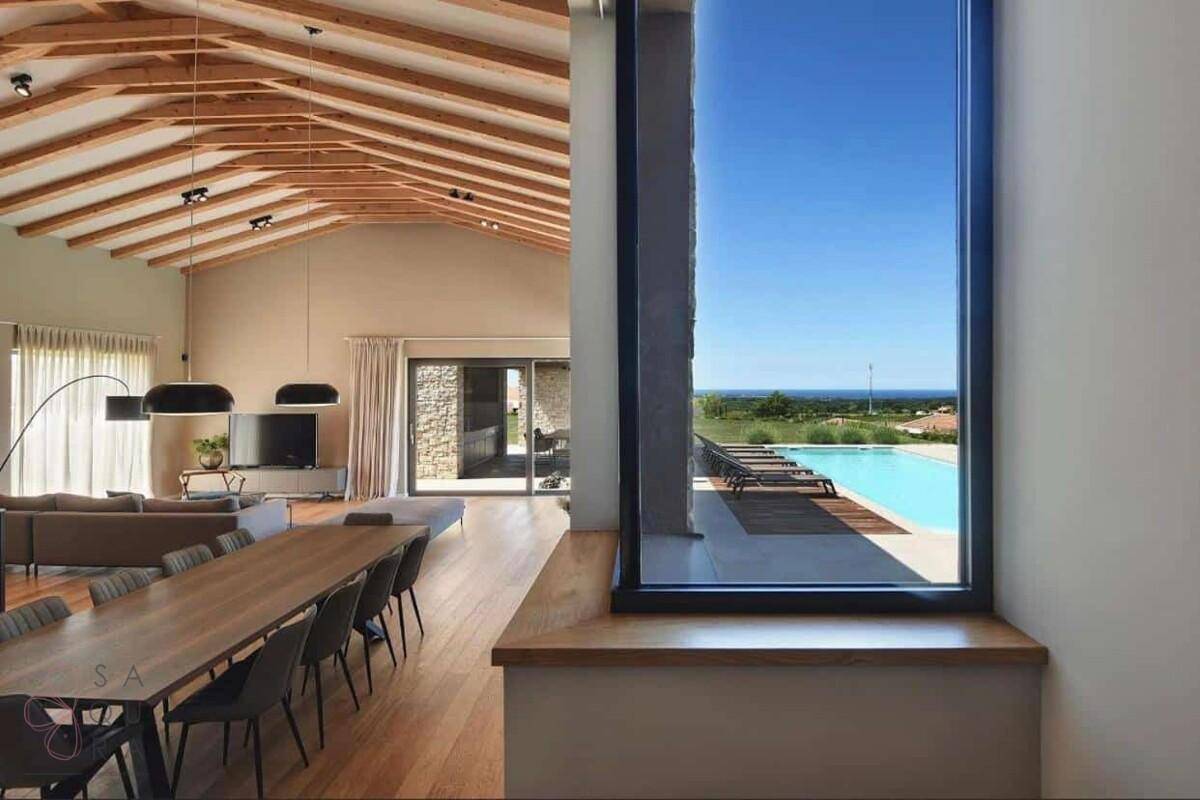 Geräumiger Wohn-Essbereich mit hohen Holzdecken, großen Fenstern und Panoramablick auf Pool und Meer.