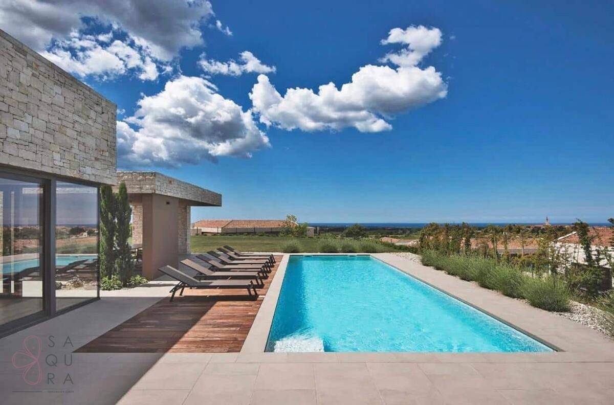 Rechteckiger Swimmingpool mit Holzdeck und weitem Blick auf die grüne Landschaft und das Meer.