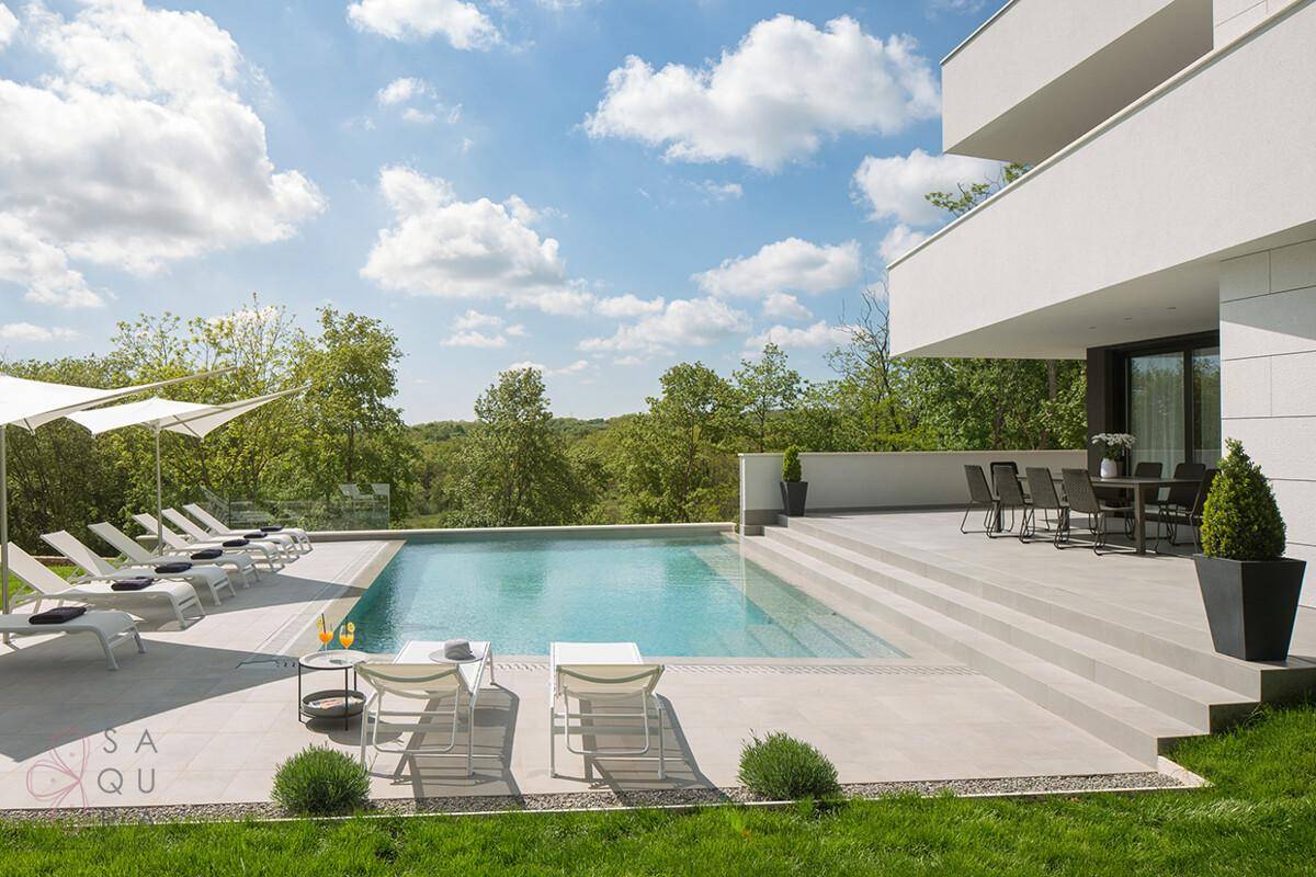 Große Sonnenterrasse mit Esstisch, Liegestühlen und Infinity-Pool vor grüner Landschaft.