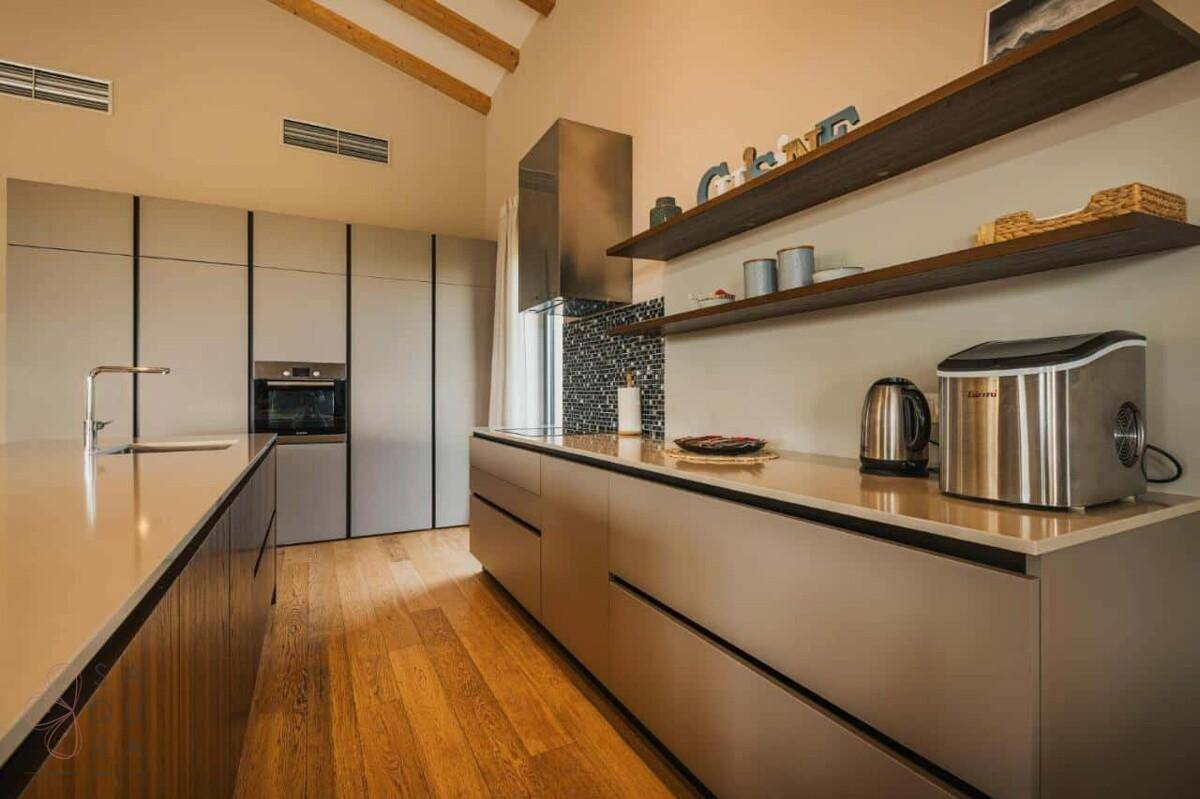 Moderne Küche mit hohen, gewölbten Decken, sichtbaren Holzbalken, hochwertigem Parkettboden und integrierten Geräten.