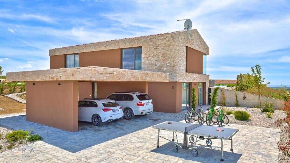 Moderne Villa mit Steinfassade, Carport und Außenbereich mit Tischtennisplatte und Fahrrädern.
