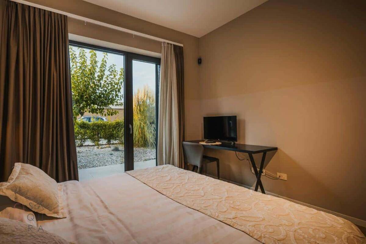 Schlafzimmer mit Doppelbett, Schreibtisch und direktem Zugang zum Garten durch eine Glasschiebetür.