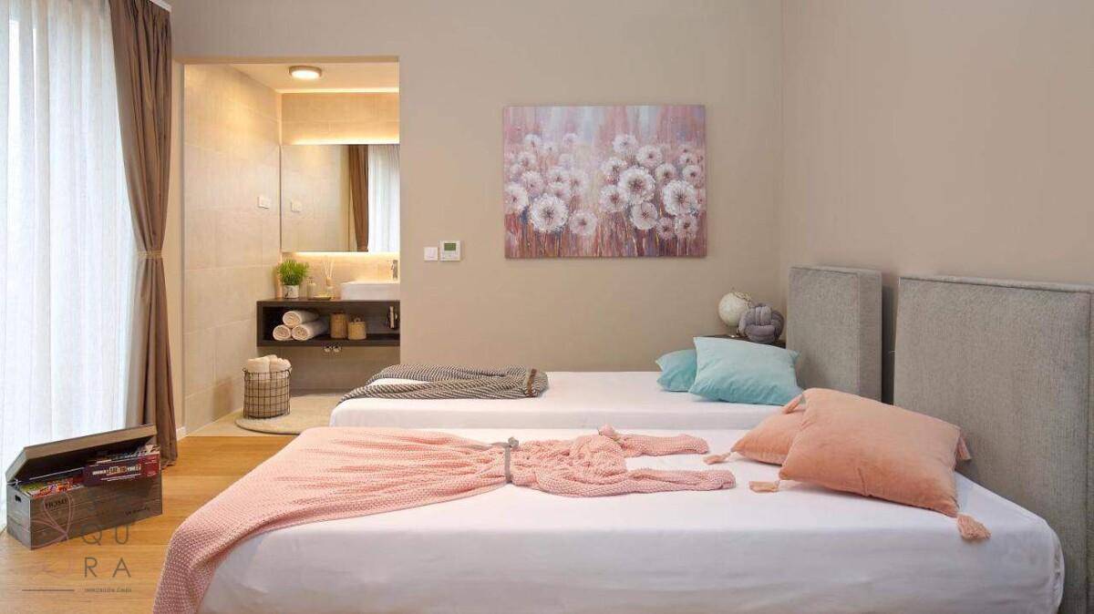 Schlafzimmer mit zwei Einzelbetten, farbigen Decken und angrenzendem modernen Badezimmer.