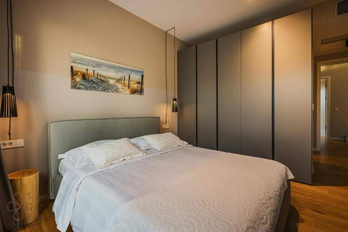 Helles Schlafzimmer mit Doppelbett, Holztisch und großem, modernem Einbauschrank.