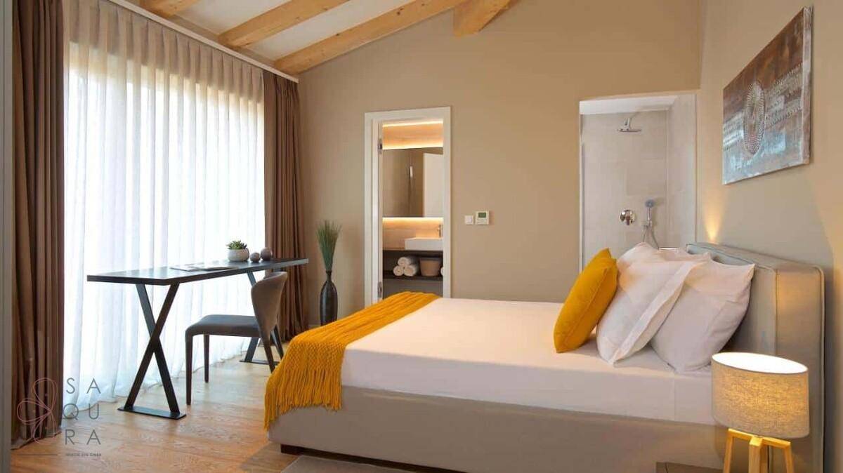 Helles Schlafzimmer mit Holzbalkendecke, Schreibtisch und direktem Zugang zu einem Duschbad.