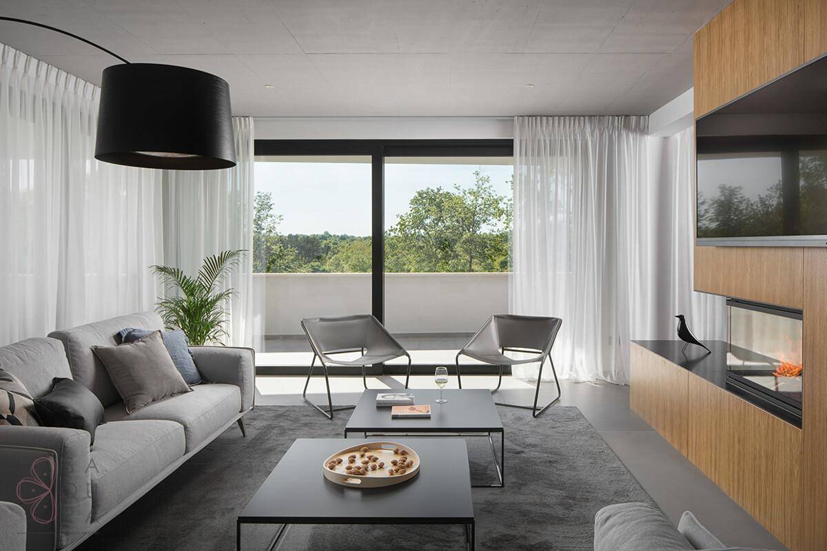 Helles Wohnzimmer mit modernem Kamin, bequemen Sofas und großen Fenstern mit Blick ins Grüne.
