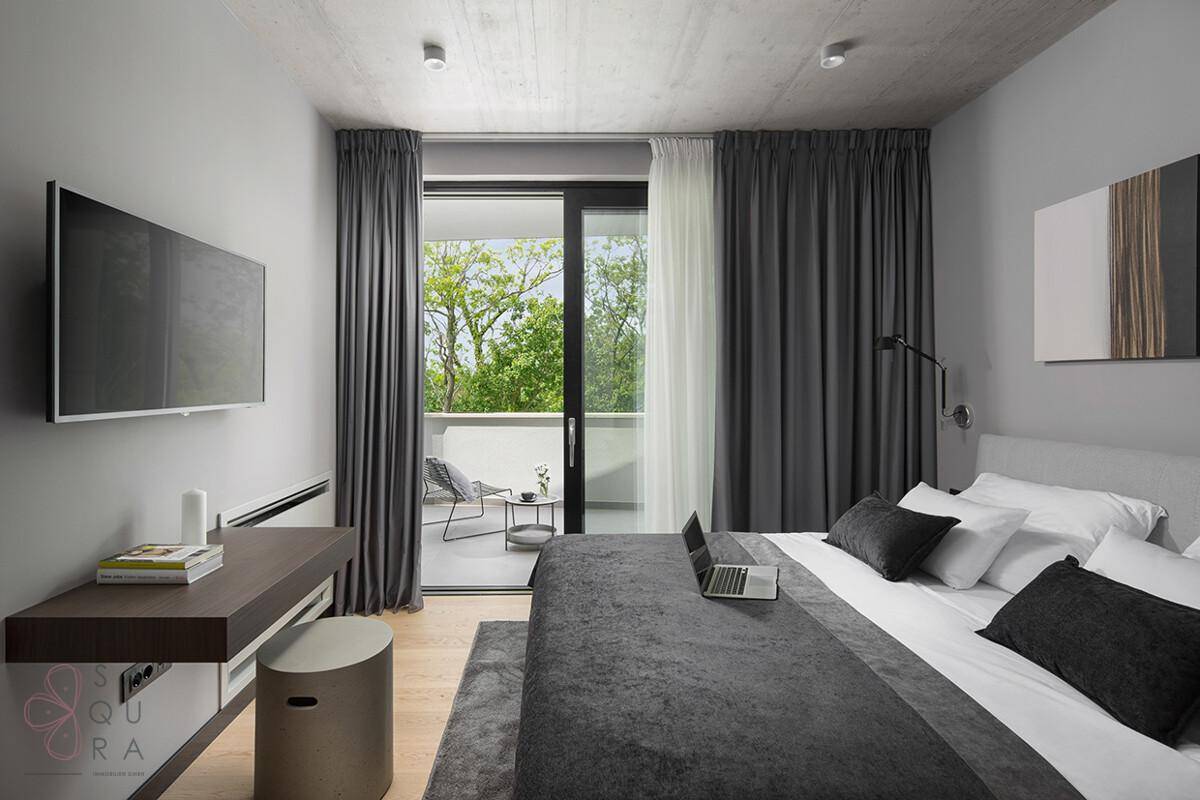 Helles Schlafzimmer mit Doppelbett, Schreibtisch und Balkonzugang mit Blick ins Grüne.