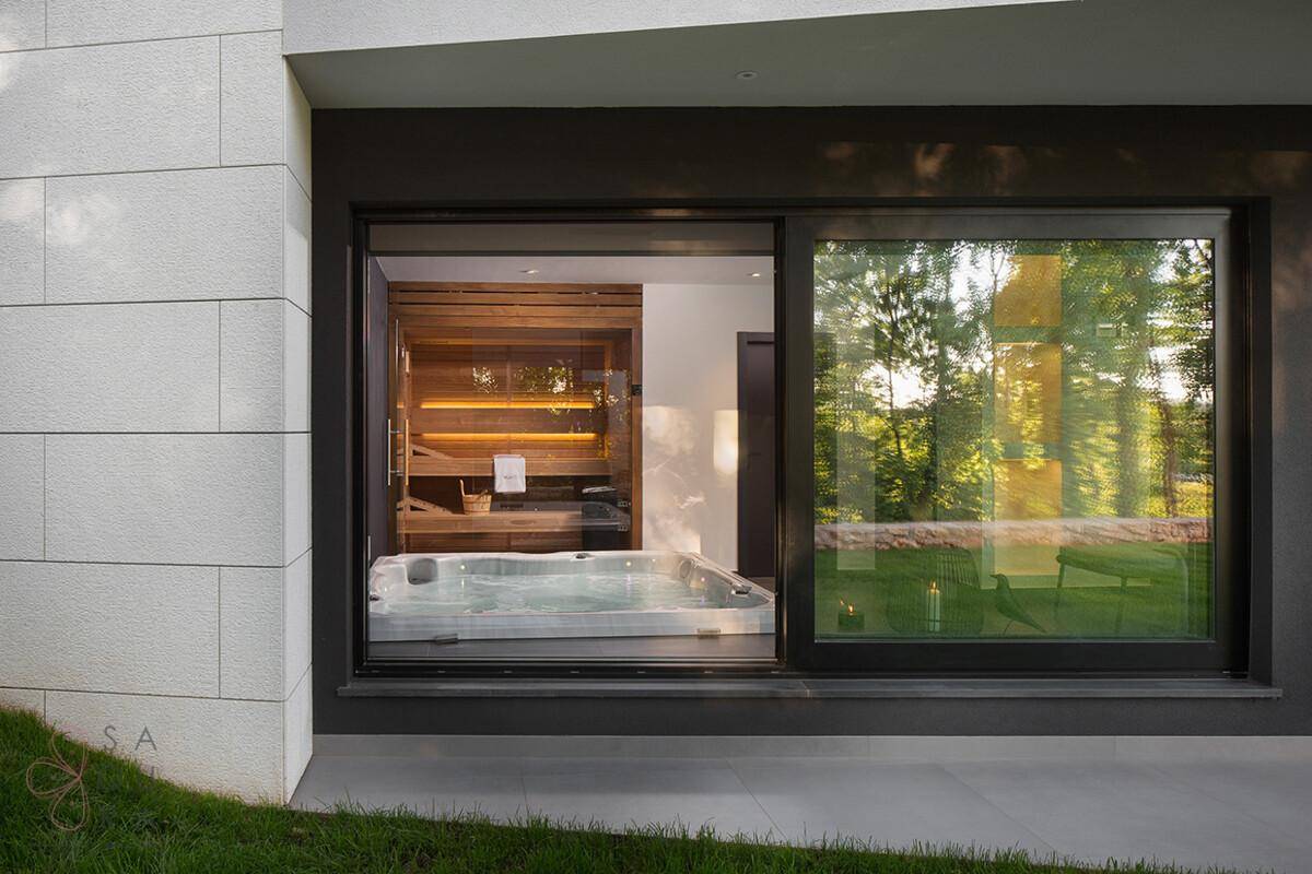 Außenansicht der Villa mit großem Fenster, das den Blick auf Whirlpool und Sauna freigibt.