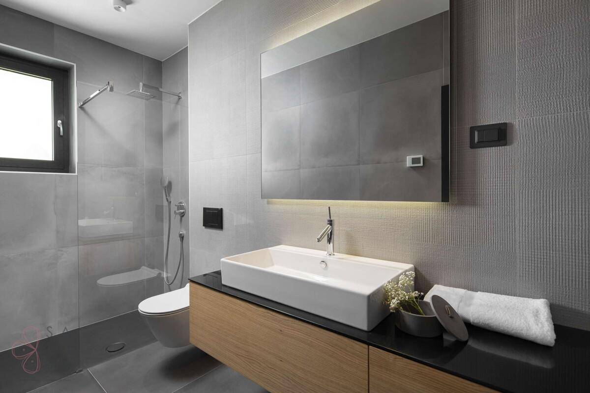 Modernes Badezimmer mit großformatigen Fliesen, wandhängendem WC und begehbarer Dusche.
