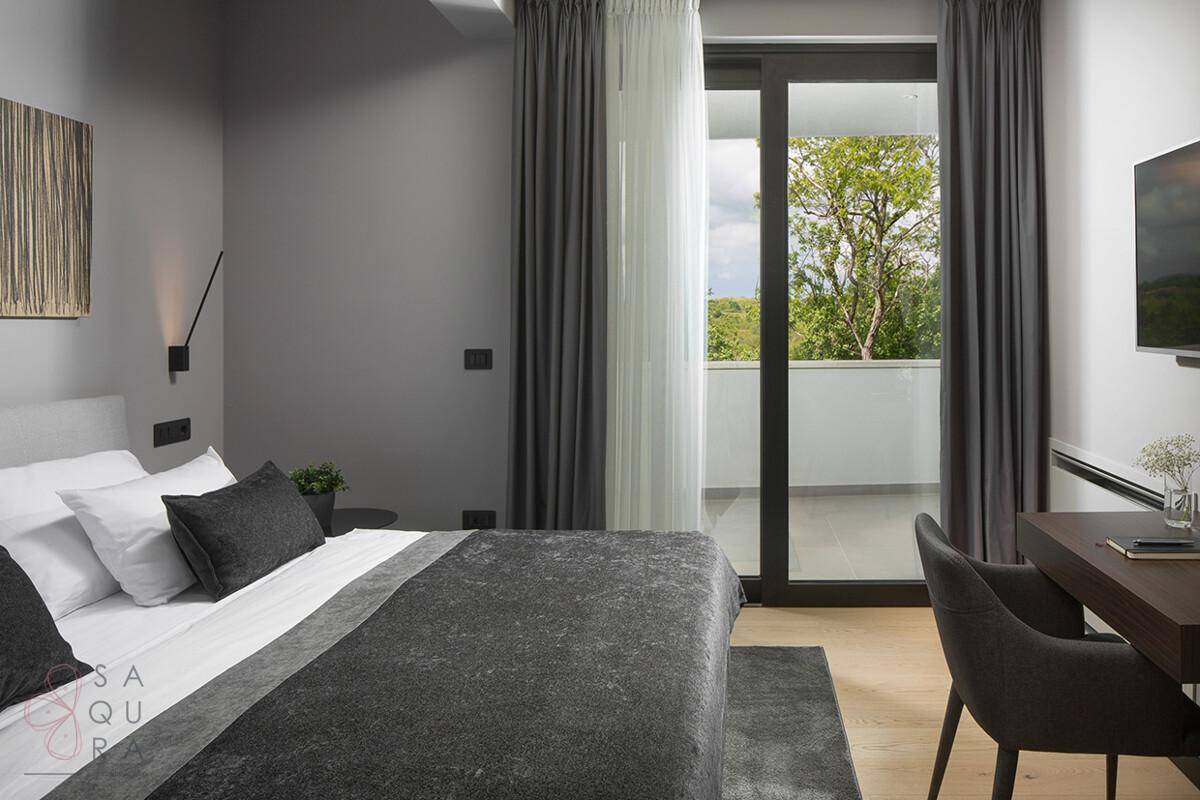 Helles Schlafzimmer mit Doppelbett, Schreibtisch und Balkonzugang mit Blick ins Grüne.