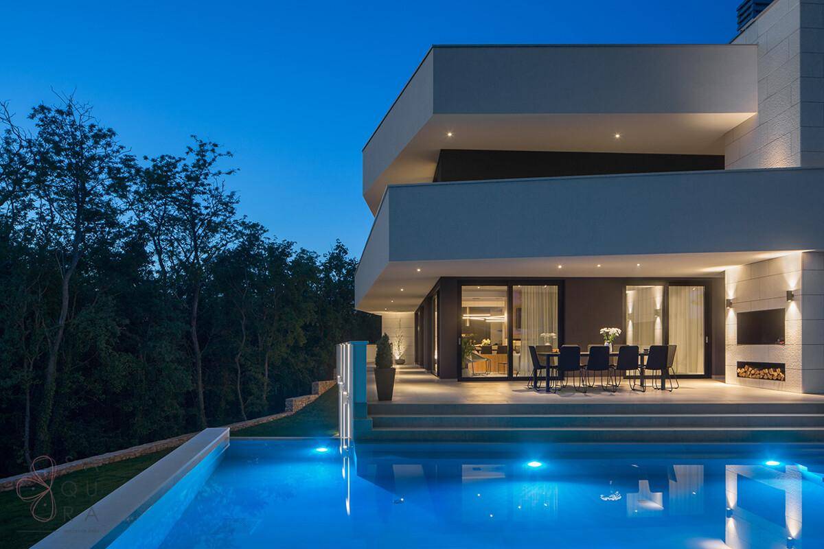 Luxuriöses modernes Anwesen mit beleuchtetem Pool und großzügiger Terrasse für entspannte Abende.