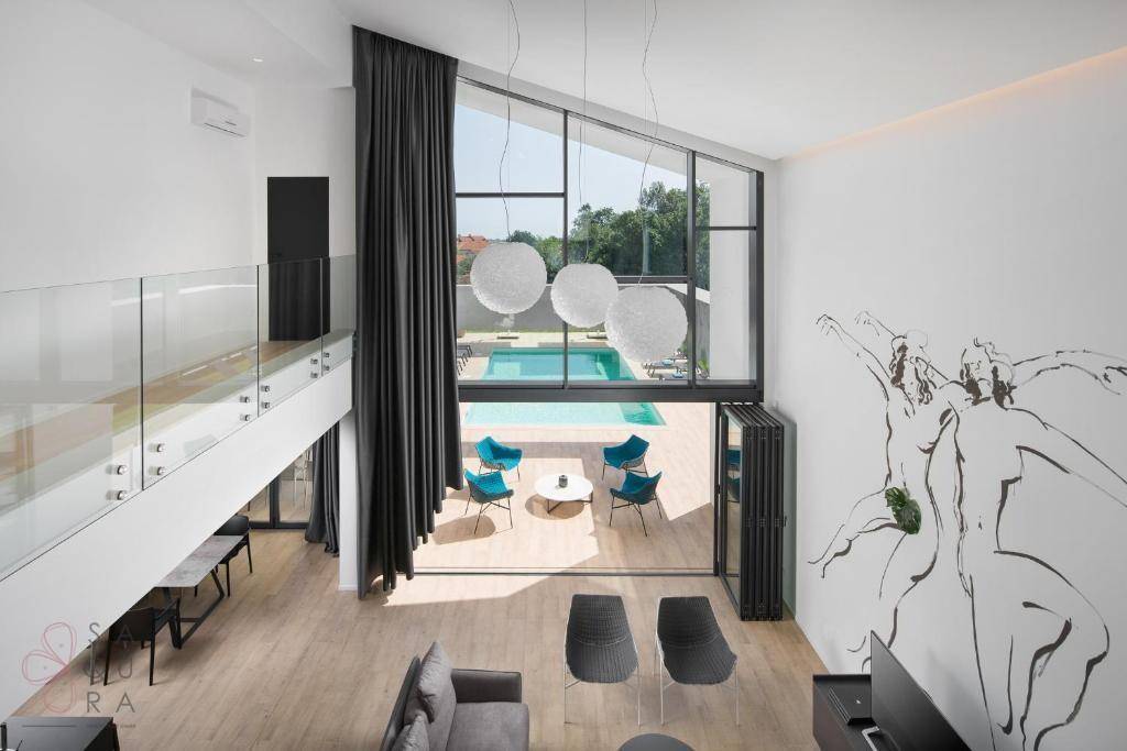 Blick von der Galerie auf das Wohnzimmer mit hohen Fenstern und direktem Zugang zum Poolbereich.