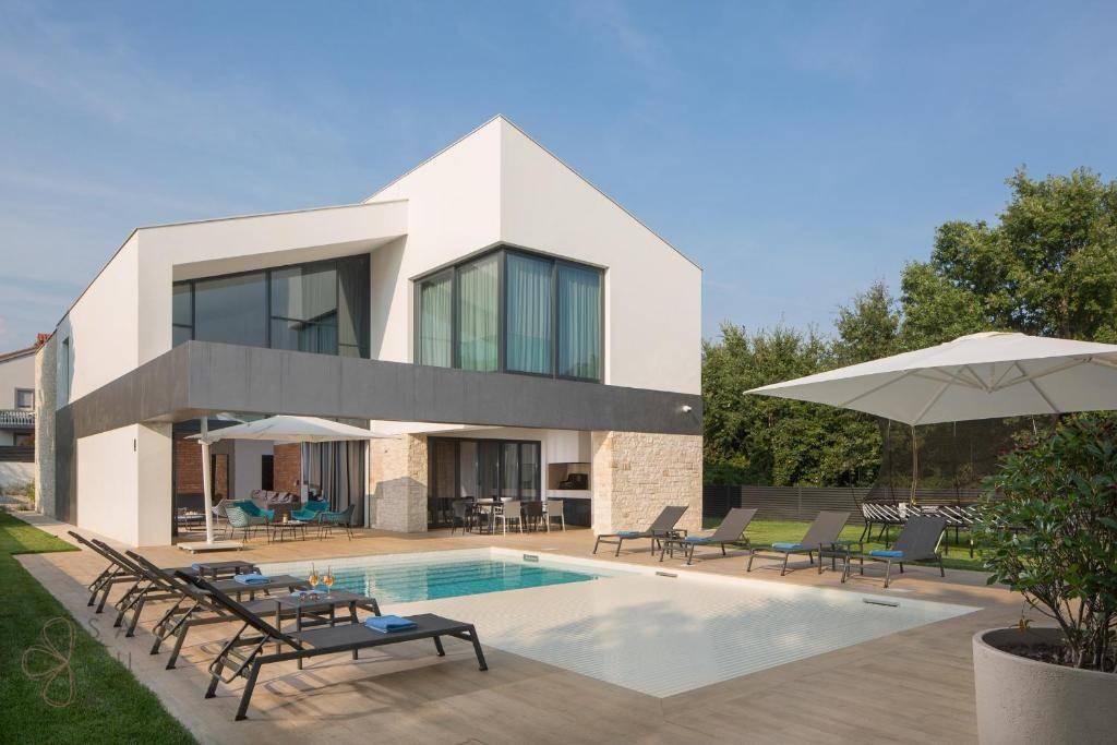 Luxuriöse Villa mit großem Swimmingpool, Liegestühlen und Sonnenschirmen unter blauem Himmel.