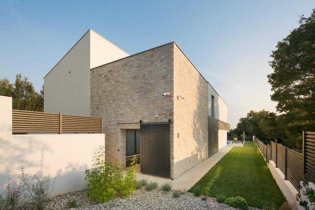 Seitenansicht der modernen Villa mit Steinverkleidung und gepflegtem Rasenbereich.