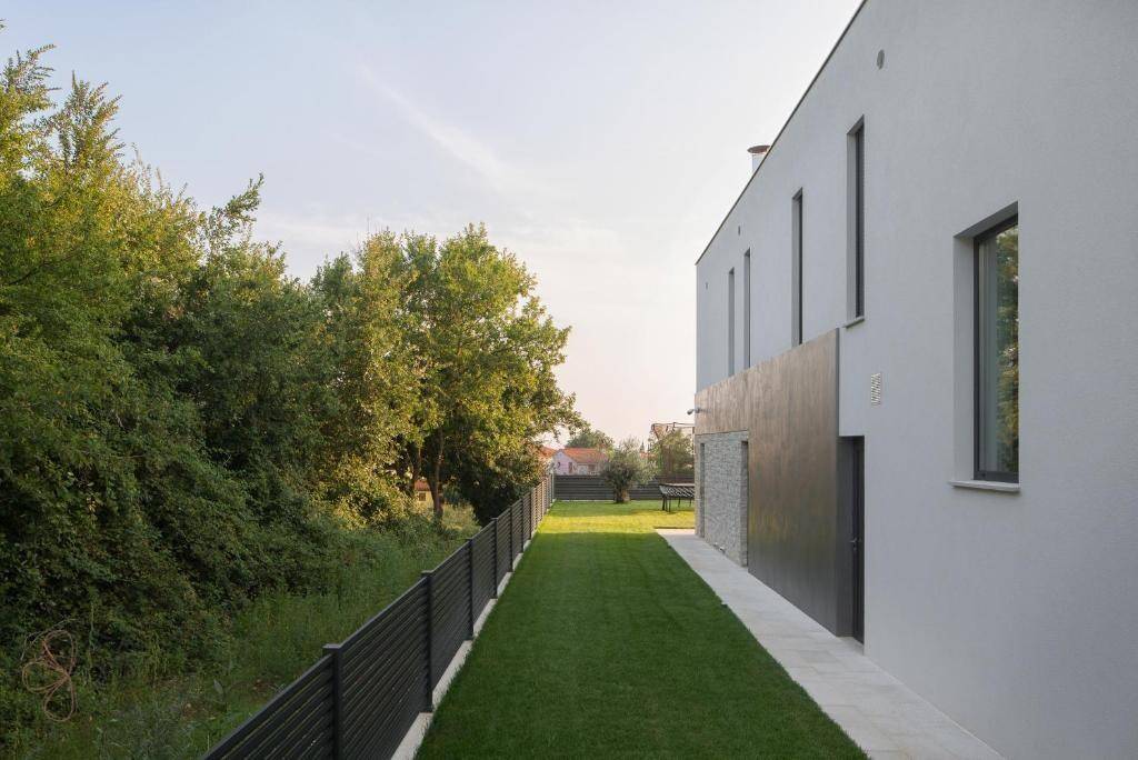 Langer, schmaler Gartenbereich entlang der modernen Hausfassade mit üppigem Grün.